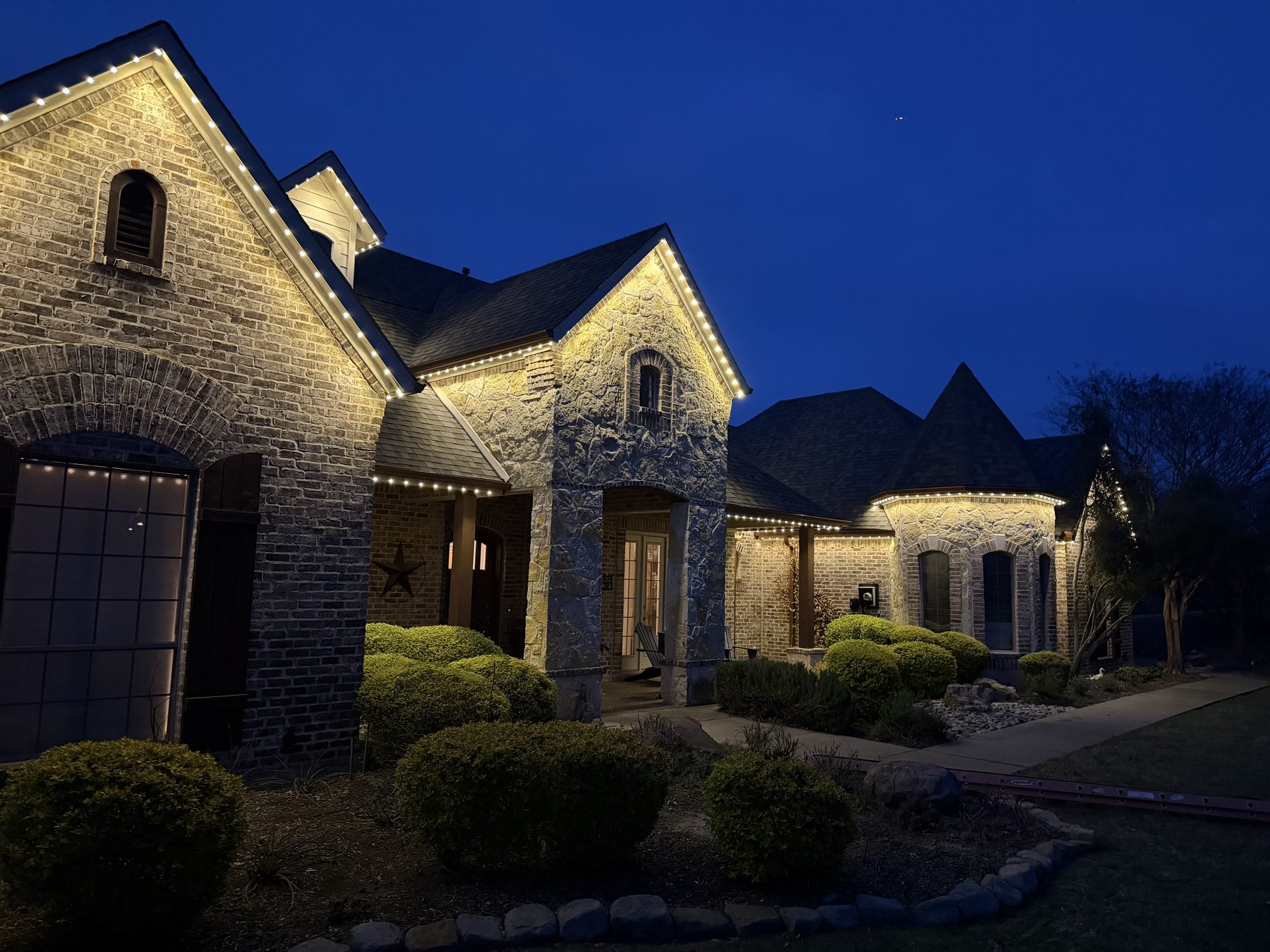 Brick and stone estate outlined in warm white permanent outdoor lighting at dusk